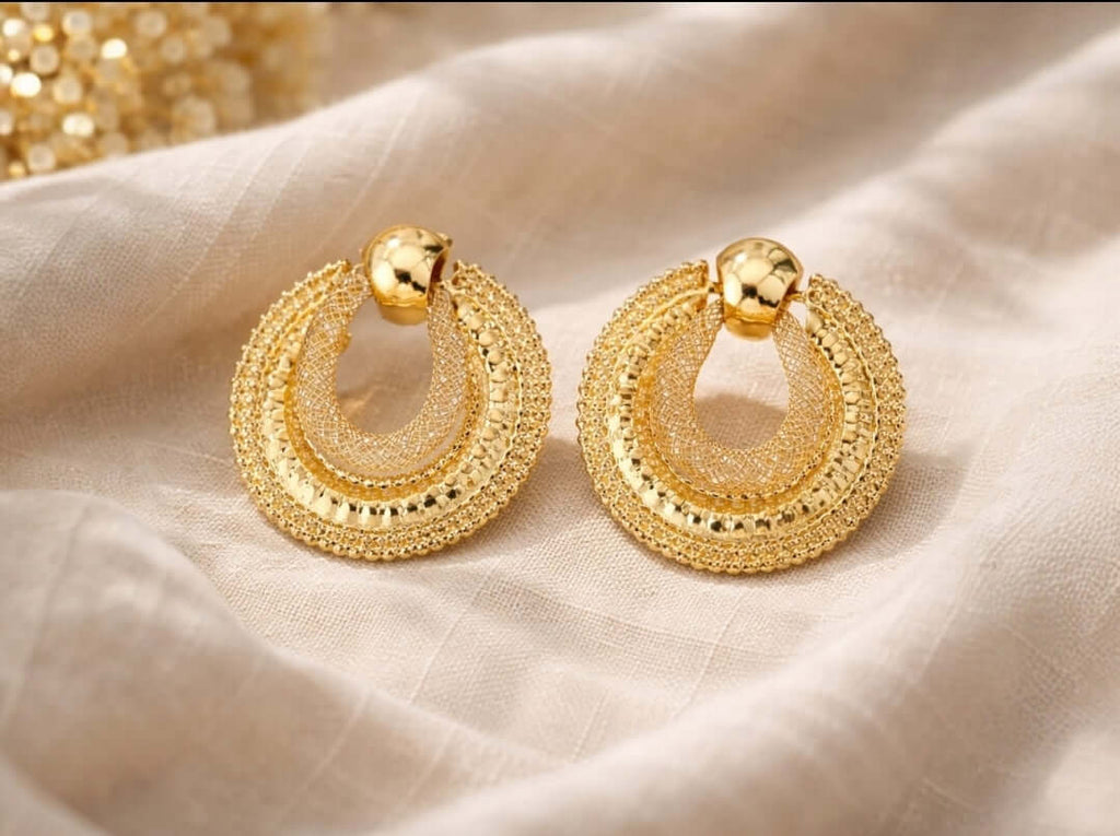 Détail des boucles d’oreilles dorées texturées en cercles superposés
