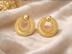 Détail des boucles d’oreilles dorées texturées en cercles superposés