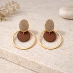 Détail des boucles d’oreilles : pastille ovale beige, disque brun mat et anneau doré