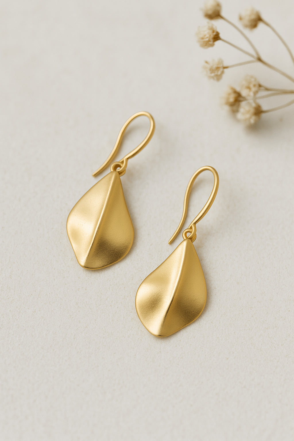Détail boucles d’oreilles dorées mates relief central style feuille