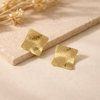 Détail texture craquelée sur boucles d’oreilles carrées finition dorée