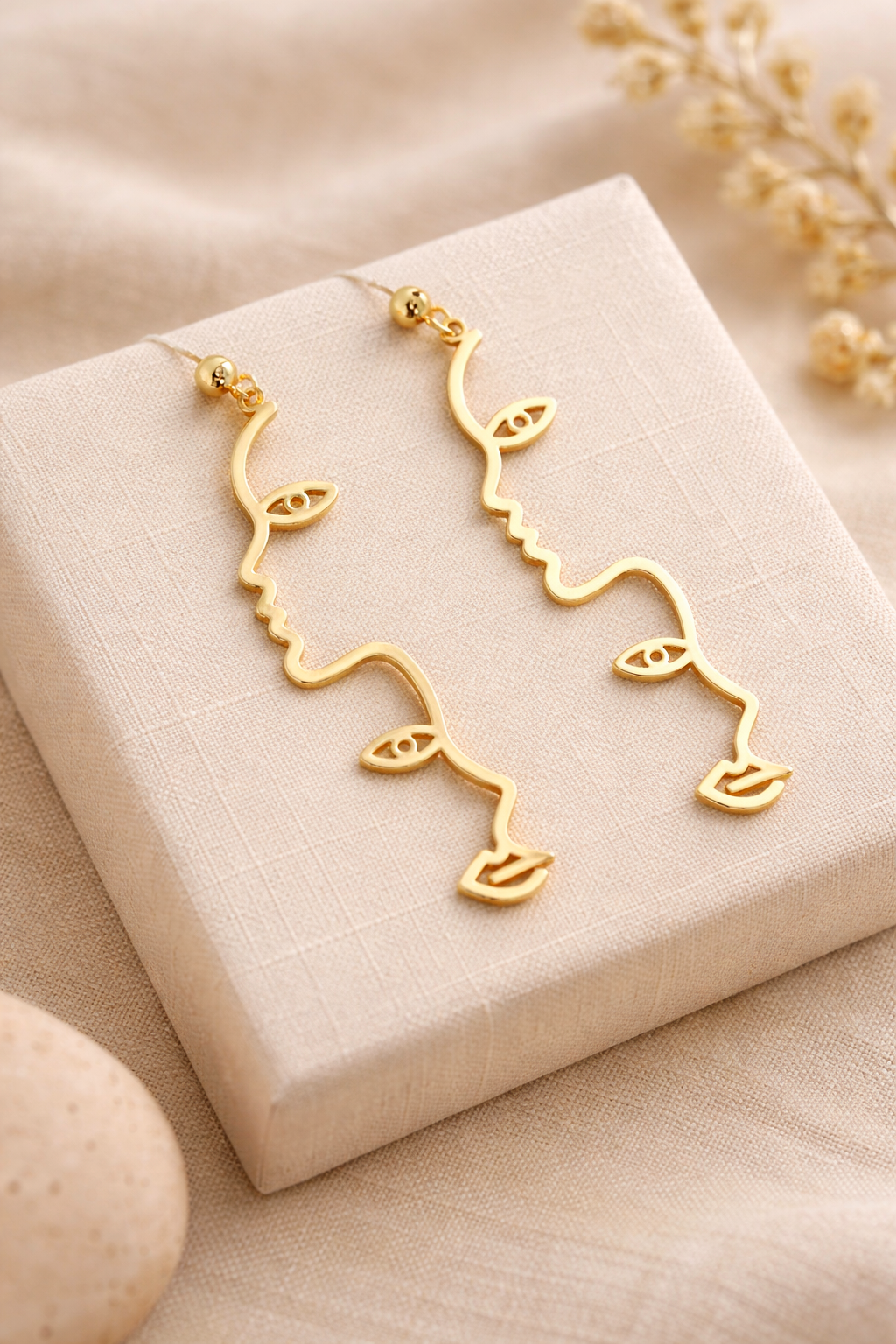 Détail boucles d’oreilles dorées forme visage abstrait avec œil et lèvres
